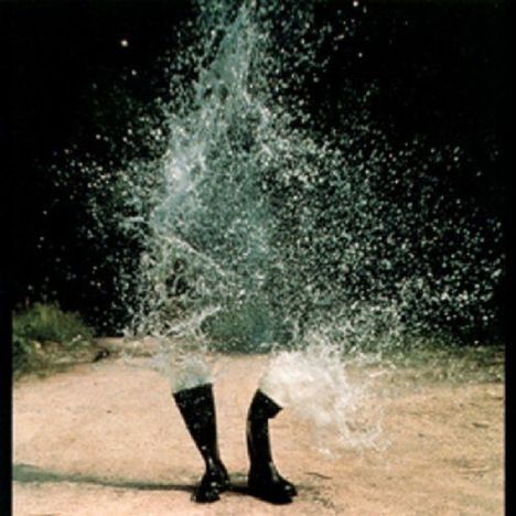 Keine erkennbaren Texte. Ein Spritzer Wasser, der von unten in die Luft schießt, schwarze Gummistiefel auf Boden.