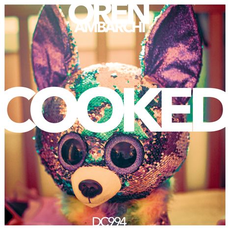 Oben "OREN AMBARCHI", groß "COOKED", unten "DC994". Darunter eine bunte, glitzernde Plüschfigur.