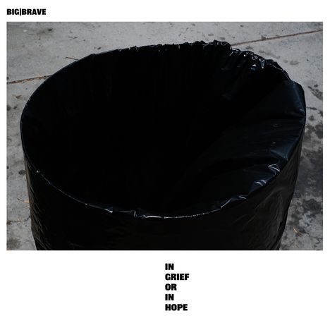 Text „IN GRIEF OR IN HOPE“, „BIG|BRAVE“. Ein leerer, schwarzer Müllsack auf einem Betonboden.