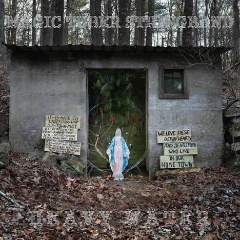 Text "MAGIC TUBER STRINGBAND" oben, "HEAVY WATER" unten. Statue der Jungfrau Maria vor grünem Hintergrund, umgeben von Blättern.