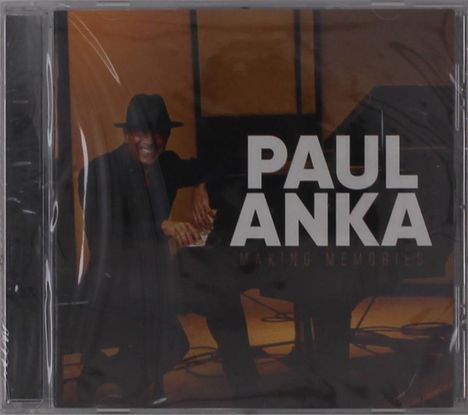 "PAUL ANKA MAKING MEMORIES" in weißer Schrift. Ein Mann mit Hut lächelt und sitzt an einem Klavier.
