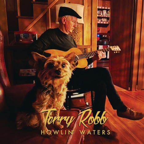 "Terry Robb, Howlin' Waters". Ein Mann spielt Gitarre in einem gemütlichen Raum, während ein kleiner Hund entspannt in die Kamera schaut.