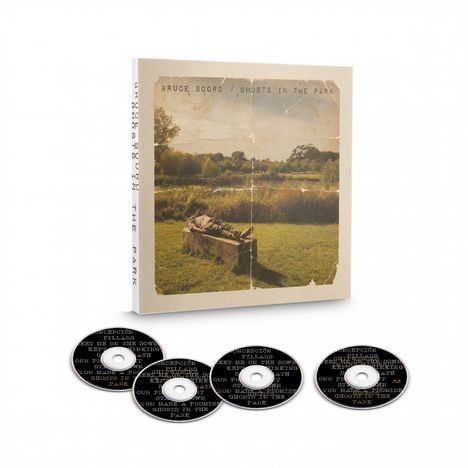 BRUCE SOORD / GHOSTS IN THE PARK. Ein Mann liegt auf einer Bank in einem Park, umgeben von grüner Landschaft und CDs.