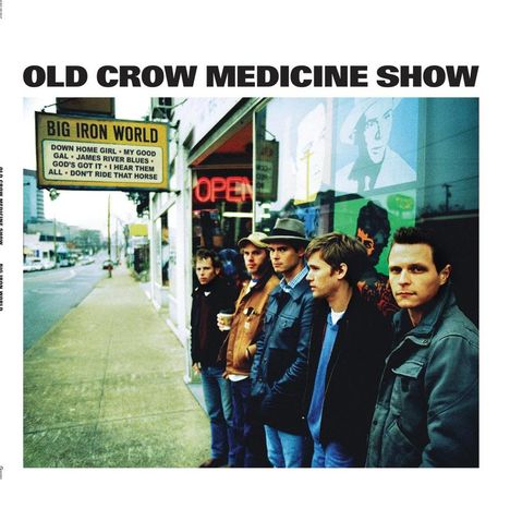 Text: "OLD CROW MEDICINE SHOW", "BIG IRON WORLD", Songtitel auf einem Schild. Fünf Männer stehen vor einem Schaufenster.