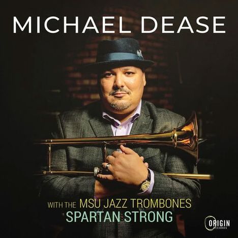 Text: "Michael Dease with the MSU Jazz Trombones Spartan Strong." Mann mit Trompete, trägt Hut und Anzug.
