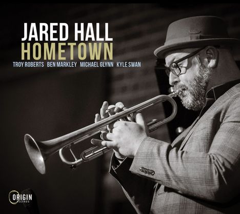 "Jared Hall Hometown" mit Musikernamen. Ein Mann spielt Trompete, trägt Hut und Brille, im Hintergrund Ziegelwand.