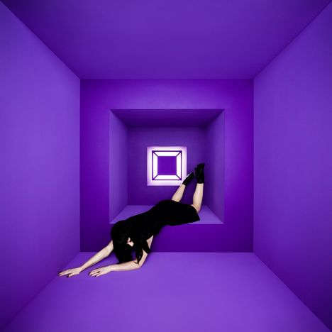 Ein Raum in kräftigem Violett, perspektivisch verzerrt. Eine Person in Schwarz lehnt an der Wand.