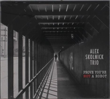 ALEX SKOLNICK TRIO, PROVE YOU'RE NOT A ROBOT. Schwarz-weißes Foto eines langen, schattigen Korridors mit einer Person.