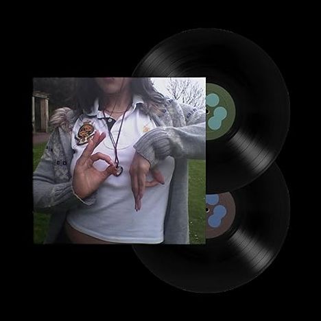 Eine Person zeigt Handgesten. Zwei Schallplatten sind sichtbar. Das Bild hat keinen erkennbaren Text.