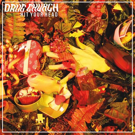 „Drug Church - Hit Your Head“ steht oben. Ein chaotisches Stillleben mit Pflanzen, Spielzeug und dekorativen Objekten.