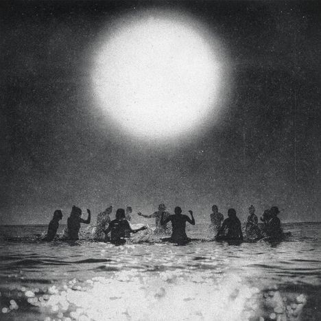 Schwarz-Weiß-Szene von Menschen beim Baden im Meer, große helle Sonne am Himmel.