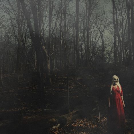 Eine Frau mit langem, hellem Haar und Skelett-Make-up steht in einem dunklen, kahlen Wald und trägt ein rotes Kleid.