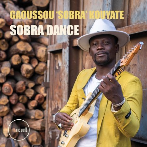 Texte: "GAOUSSON 'SOBRA' KOUYATE", "SOBRA DANCE".  
Mann in gelbem Sakko mit Gitarre, lächelt, Holzstapel im Hintergrund.