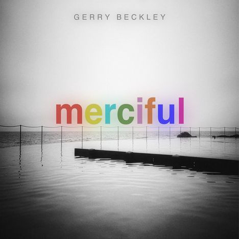 Text "merciful" in Regenbogenfarben, darüber "Gerry Beckley". Im Hintergrund ein ruhiges, graues Meer.