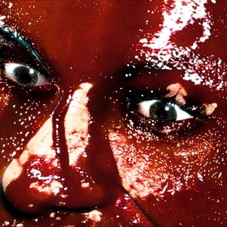 Ein Gesicht mit intensivem, glitzerndem roten Licht- und Schattenspiel, das die Augen stark hervorhebt.