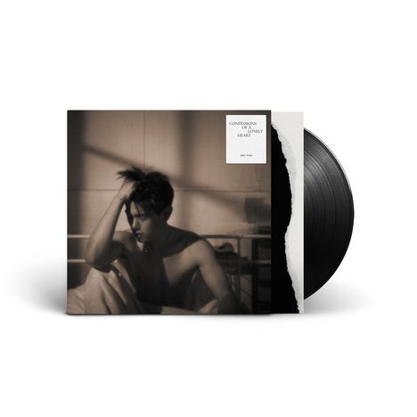 Text: "CONFESSIONS OF A LONELY HEART", "ERIC NAM". Schwarz-weiß Bild, Mann sitzt nachdenklich auf Bett.
