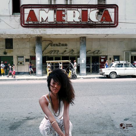 Großes Schild mit „AMÉRICA“, darunter „Teatro América“, Frau mit lockigem Haar im Fokus, Straße, alte Autos.