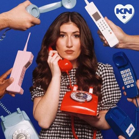 Herzlogo mit "KN" und Stern. Frau mit rotem Telefon, umgeben von alten Telefonen, blickt ernst.