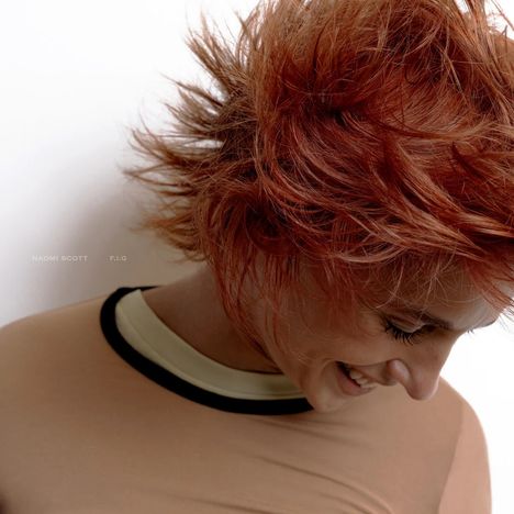 Naomi Scott, F.I.G. Frau mit rotem, zerzaustem Haar lacht und schaut nach unten, trägt ein beiges Oberteil mit dunklem Kragen.