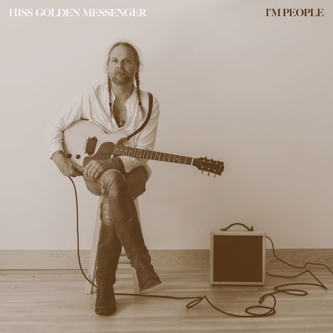 Texte: "HISS GOLDEN MESSENGER" oben links, "I'M PEOPLE" oben rechts. Ein Mann mit Gitarre sitzt lässig auf einem Hocker.
