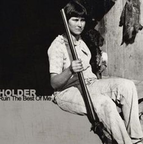 Text: "HOLDER" und "Ruin The Best Of Me". Eine Person sitzt mit einem Gewehr vor einem Gebäude. Schwarzweißfoto.