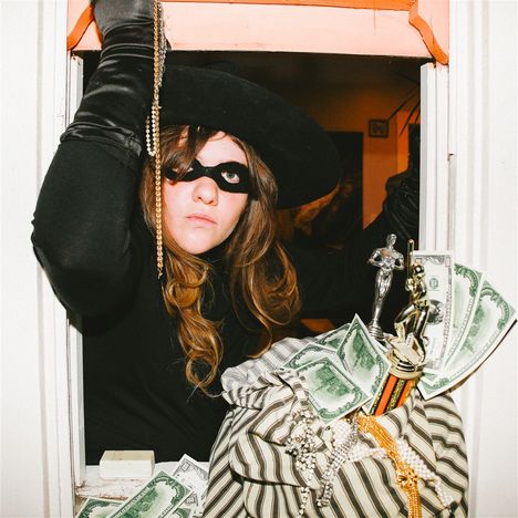 Eine Person in schwarzem Kostüm mit Hut und Maske, umgeben von Schmuck, Trophäen und Spielgeld in einem gestreiften Sack.