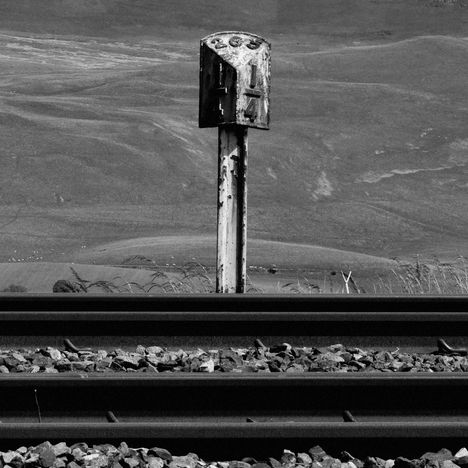 Alte, verwitterte Bahnkilometertafel mit der Zahl 266 an Bahngleisen vor hügeliger Landschaft. Schwarz-weiß.