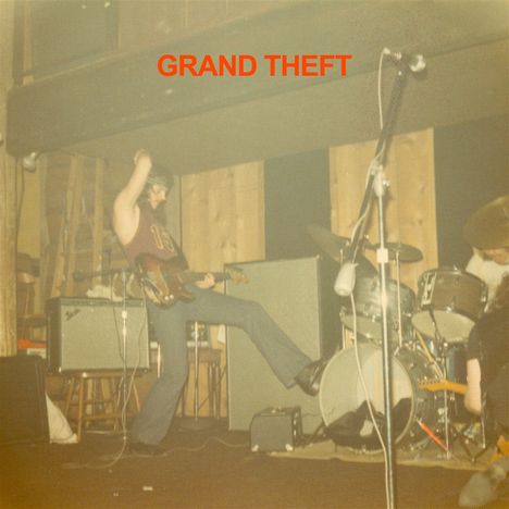 Text "GRAND THEFT" in Rot oben. Eine Band spielt energetisch auf einer Bühne mit Gitarre und Schlagzeug.