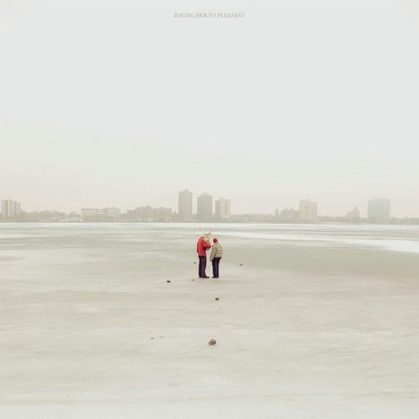 Text: "Racing Mount Pleasant". Zwei Personen auf einer vereisten Fläche, im Hintergrund eine entfernte Skyline.