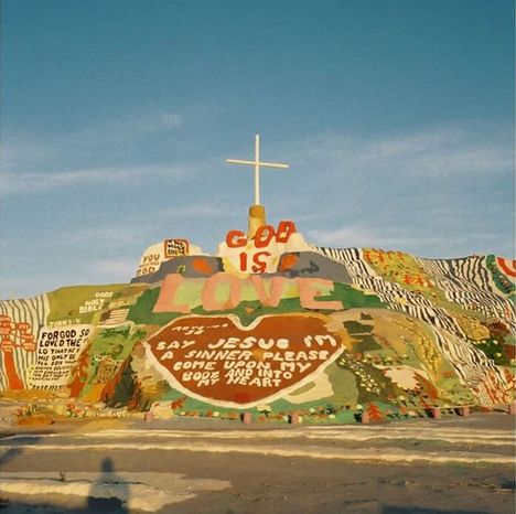 Bunte, bemalte Hügel mit Texten: "God is Love", "Say Jesus, I'm a sinner...", oben ein großes Kreuz, viele weitere bunte Botschaften.