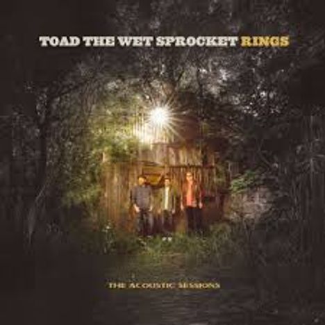 Oben steht "TOAD THE WET SPROCKET RINGS". Unten "THE ACOUSTIC SESSIONS". Drei Personen vor einer Hütte im Wald.