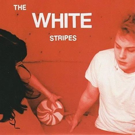 „THE WHITE STRIPES“ in Weiß. Zwei Personen, eine hält einen rot-weißen Ball, die andere trägt ein weißes Shirt.