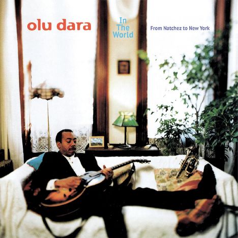 "Olu Dara", "In The World", "From Natchez to New York". Ein Mann mit Gitarre entspannt auf einem Sofa, umgeben von Pflanzen.