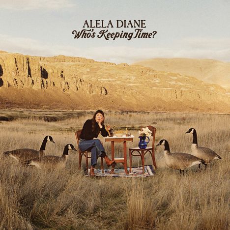 Text: "Alela Diane, Who's Keeping Time?" Frau sitzt an Tisch in Wiese, umrahmt von Gänsen, im Hintergrund felsige Landschaft.
