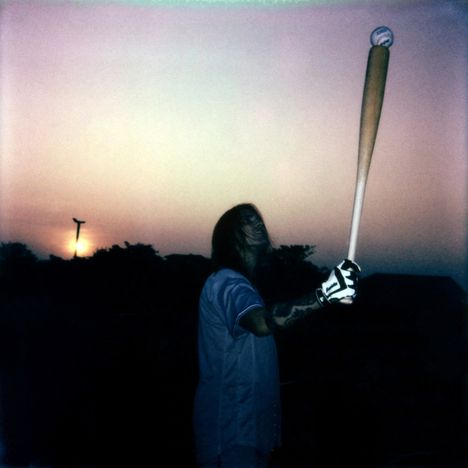 Eine Person hält einen Baseballschläger mit einem Ball darauf, im Hintergrund ein Sonnenuntergang.