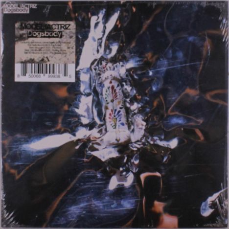 Text: "MODEL/ACTRIZ Dogsbody". Verpackung mit glänzender, verknitterter Oberfläche, bunt verzierte Keramikkatze in der Mitte.