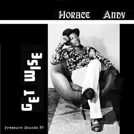 „Horace Andy – Get Wise“. Schwarz-Weiß-Foto: Mann in Hut und gemustertem Hemd sitzt lässig in einem Sessel.