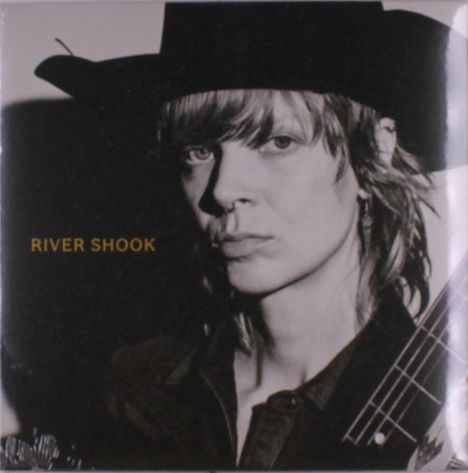 Text: RIVER SHOOK. 
Schwarz-weiße Fotografie einer Person mit Hut blickt ernst.