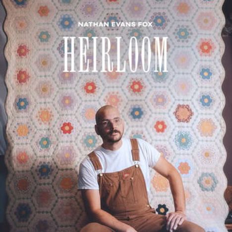 Text: "NATHAN EVANS FOX" und "HEIRLOOM". Ein Mann mit Brille und Latzhose sitzt vor einer Patchworkdecke mit bunten Mustern.