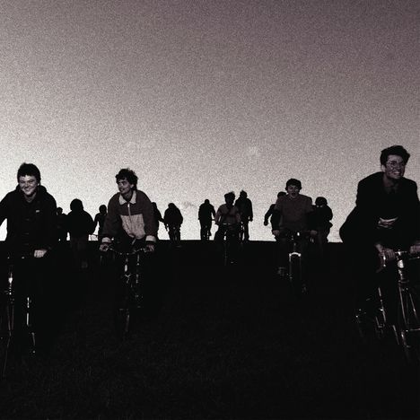 Ich kann darauf nicht viel Text erkennen. Mehrere Menschen fahren fröhlich auf Fahrrädern den Hügel hinunter.