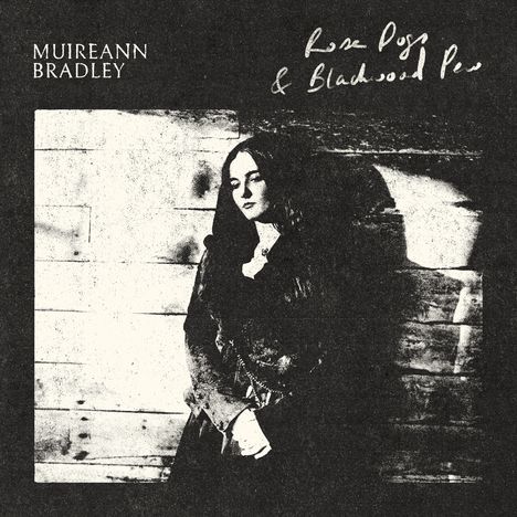 Text: „Muireann Bradley, Rose Dogs & Blackwood Pews“. Frau lehnt an Holzwand, monochrom, Schatten.