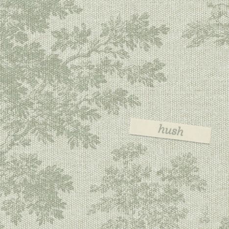 Der Text "hush" ist auf einem Etikett zu sehen, platziert auf einem stoffähnlichen Hintergrund mit floralem Muster in Grün.