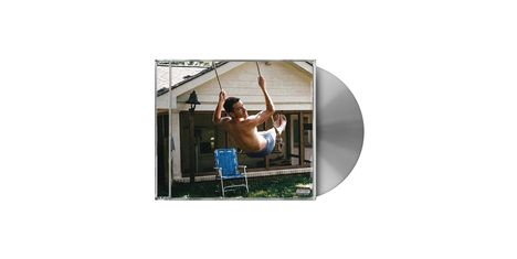 Ein Mann schaukelt ohne Hemd im Garten vor einem Haus. Ein blauer Stuhl steht darunter. Ein "Parental Advisory"-Logo ist zu sehen.