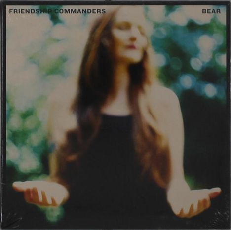 Oben steht "FRIENDSHIP COMMANDERS" und "BEAR". Verschwommene Frau mit langen Haaren, Arme ausgestreckt, grüner Hintergrund.