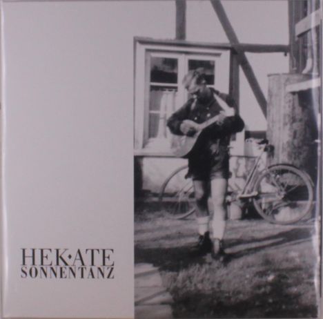 Text: HEKATE SONNENTANZ. Schwarz-weißes Foto: Person spielt Gitarre, Fahrrad und Fachwerkhaus im Hintergrund.