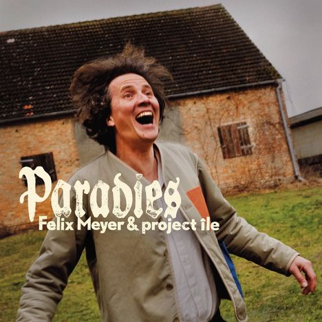 „Paradies, Felix Meyer & project île“. Ein lachender Mann in einem Hof vor einem alten Gebäude.