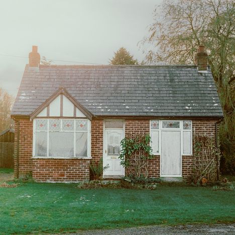 Ein kleines Ziegelhaus mit grauem Schieferdach, grüner Vorgarten mit Pflanzen, Fenster mit roten Akzenten.