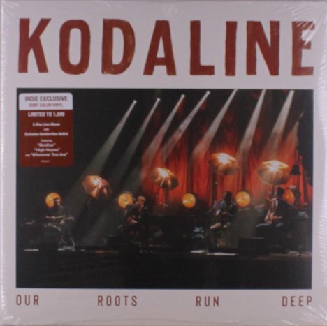 "Kodaline", "Our Roots Run Deep". Indie Exclusive Hinweis. Bühne mit Musikern, warme Beleuchtung und rote Vorhänge.
