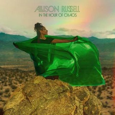 ALISON RUSSELL, IN THE HOUR OF CHAOS. Eine Frau steht auf Felsen in der Wüste, trägt ein weites, grünes Tuch.