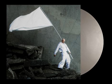 Ein Mann in weißem Anzug hält eine große weiße Flagge, steht vor Beton und Schutt. Neben ihm eine Vinyl-Schallplatte.